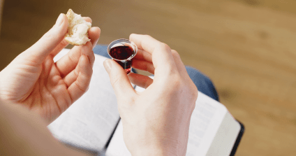 over-the-shoulder-closeup-shot-of-a-woman-holding-communion-elements-over-an-open-bible_bzg4p9jr__F0000